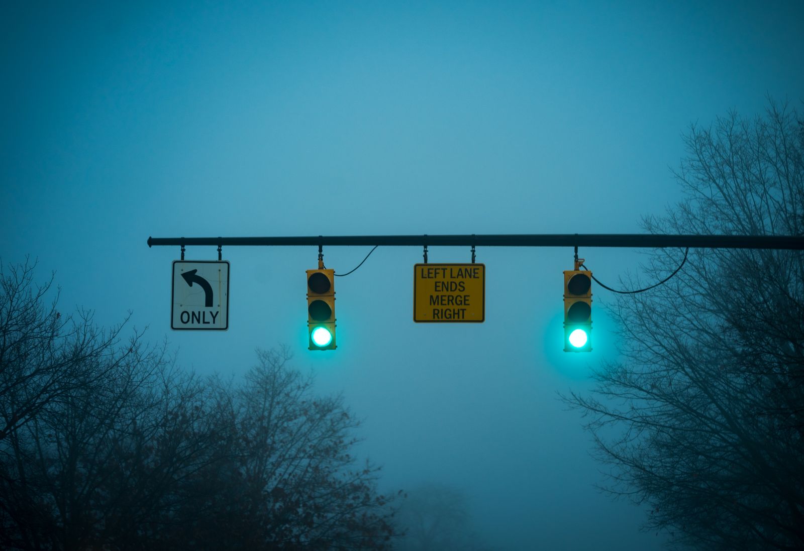 Two green traffic lights on a misty evening